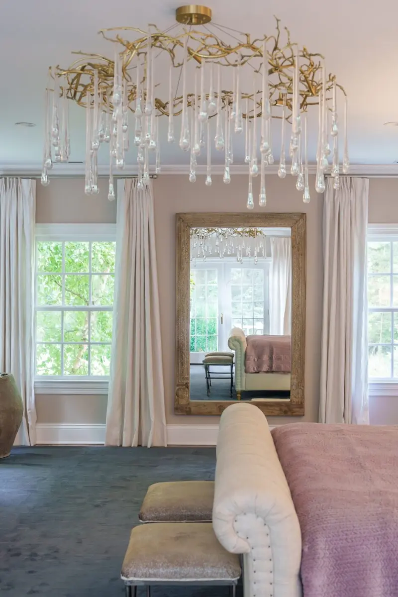 Bedroom with a branch-form crystal chandelier, floor-length curtains and a gilt-framed mirror, designed by Beth Krupa Interiors